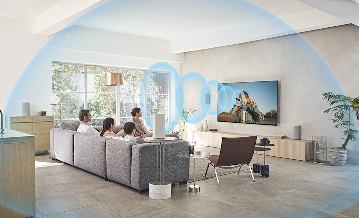 一家人坐在沙發上看電視，HT-A9 家庭影院系統置於木櫃上，螢幕傳出聲波。