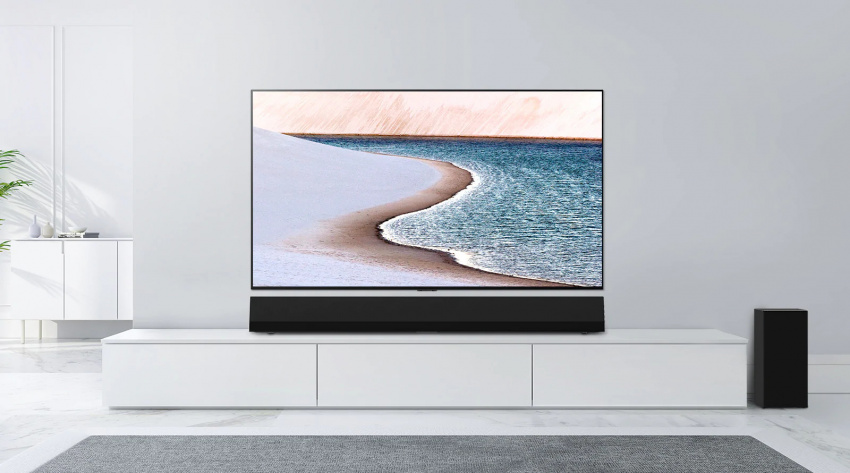 電視安裝在淺灰色牆壁上。LG Soundbar 放置在下方的白色櫃子。電視展示出一個海灘。
